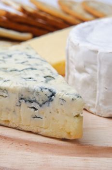 Close up of cheese selection on wooden board with crackers in soft focus background.  Focus is on French blue veined cheese.