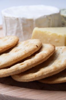 Close up of a board of crackers with cheese selection in soft focus in background.  Shallow depth of field.