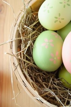 Overhead close up shot of hand painted Easter eggs nestling in straw in a basket on a wooden table.  Portrait orientation.