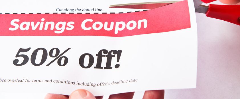 Scissors cutting dotted line of a 50% off savings coupon.  Hands visible.