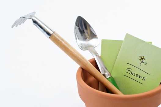 Close up of a terracotta plant pot containing seed packet and potting tools.