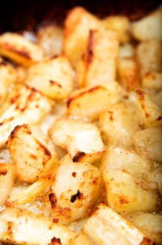 Crispy roast potatoes and parsnips in hot, bubbling oil.  Vertical (portrait) orientation.