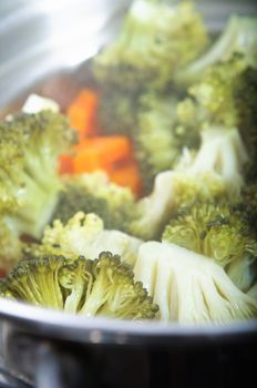 Broccoli florets and carrots cooking in a steamer, with steam visible.  Vertical (portrait) orientation.