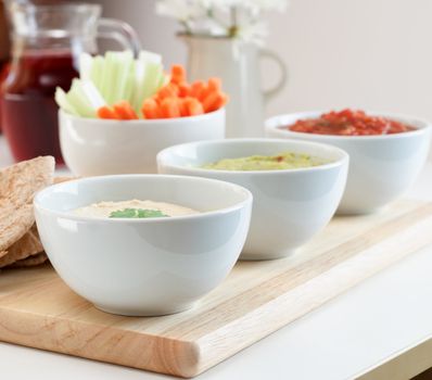 A variety of dips, with pitta bread, crudites and juice on a table.  