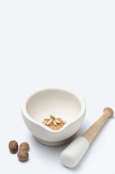 A stoneware pestle and mortar with nutmeg, cardamon and mustard seeds.  Vertical (portrait) orientation with copy space above.
