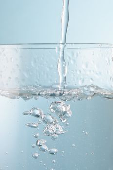 Vertical action shot of water pouring into a glass against an icy blue background.  Close up (macro).