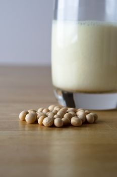 Dry soya (soy) beans with glass of soya milk in soft focus background on a light wooden table.