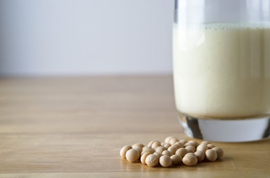 Dry soya (soy) beans with glass of soya milk in soft focus background on a light wooden table.  Horizontal (landscape) orientation.