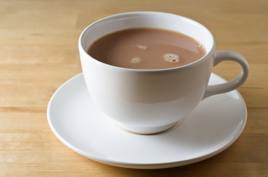 A cup of tea in white china cup and saucer on a light wooden (birch) table.  Landscape (horizontal) orientation.