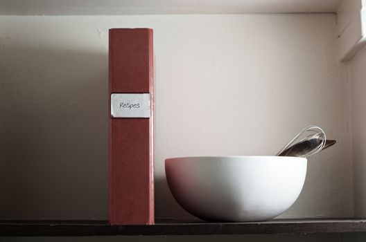 A slightly battered recipe file on an old larder shelf with mixing bowl and utensils.  Conceptual image for home cooking and family recipes.  Copy space to left and top right.