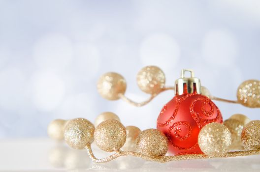 A red bauble with gold glitter balls on an 'icy' reflective surface, with blue and white snow-effect bokeh background.