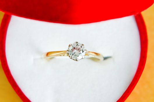 Close up (macro) of  gold, solitaire diamond engagement ring, shot from above, in an open red heart shaped box with white interior.