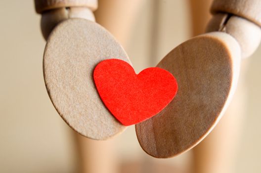 Close up (macro) of a wooden mannequin's hands, holding a red paper Valentines heart.