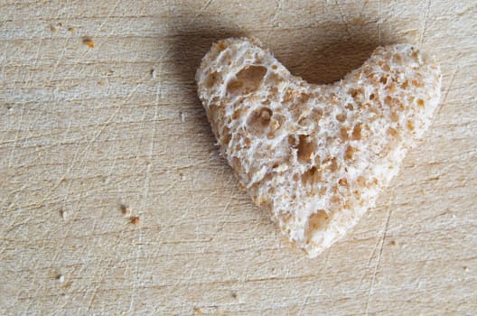 A heart of wholegrain bread, with crumbs on old wooden chopping board with cut marks visible.  Copy space on left side.