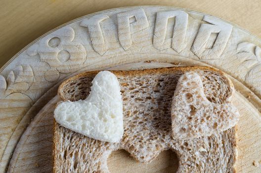 Close up of white and brown wholemeal bread hearts and slice on an old vintage bread board with the word 'bread' embossed in the wood.  