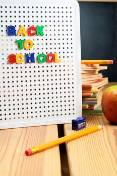A letterboard on wooden planked table with the words 'back to school' displayed, surrounded by classroom items with a blackboard in the far background.
