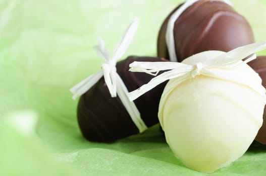 A group of home made Easter egg chocolates, bow tied with raffia ribbon, nestling on a fresh, light Spring green background.  Copy space to left.