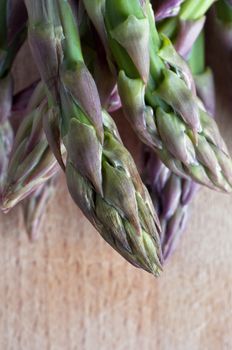 An arrangement of asparagus spears (stems) in close up (macro) on an old, scratched wooden chopping board.  Portrait orientation.