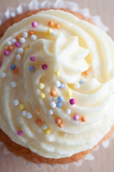 Close up (macro) of a cupcake decorated with buttercream icing and colourful sprinkles, shot from above. 