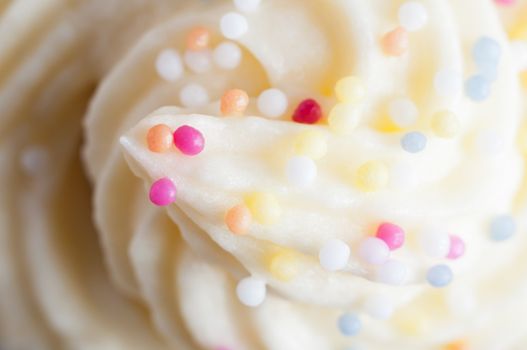 Close up (macro) of a cake topping made from swirled buttercream icing and colourful decorative sprinkles.