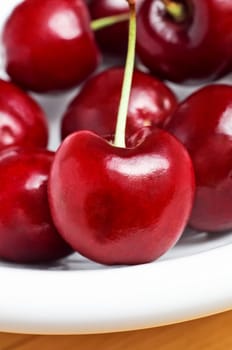 A white bowl of cherries with stalks, photographed from the front.