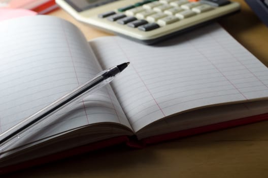 A blank, ruled, two-column cash book lying open on a wooden desk with pen resting on page.  Calculator in soft focus background.