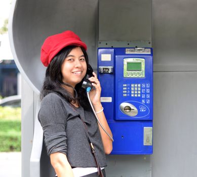 Young happy woman calling from public phone, outdoor shot 