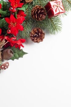 A Christmas themed border running diagonally from mid-left to upper right of frame consisting of a variety of artifical flora decorations in greens, reds and browns, with a shiny tied gift box and real fir cones.
