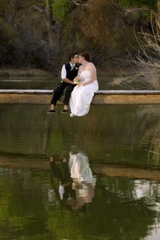 Kissing same sex newlywed on dock above lagoon