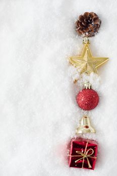 An uneven vertical line of Christmas ornaments running from top to bottom of frame, half buried in snow, on right hand side.  Copy space to left.