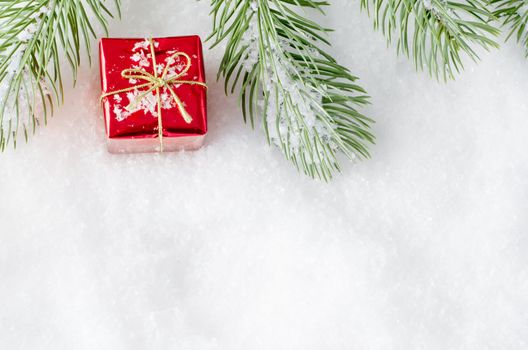 An upper frame Christmas border of artificial tree fronds on fake snow with a small shiny red gift box placed between.