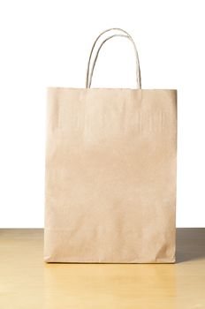 An unbranded brown paper carrier bag with twisted handles on a light wood table with white background, facing front with empty space for text.