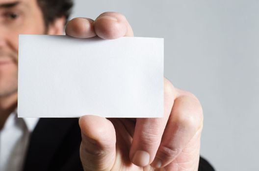 A man in a black suit with white shirt holding up a blank business card to display to viewer.