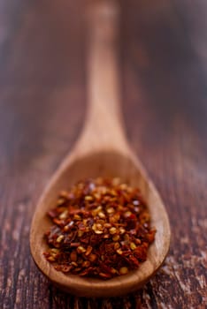 red chilli flakes in wooden spoon over wood background - selective focus