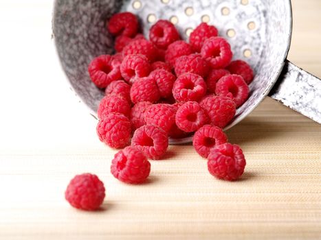 Overexposed photo of fresh raspberries spilling out of a metal colander.
