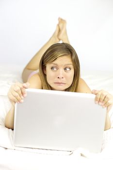 Beautiful woman making funny face laying in bed with computer 