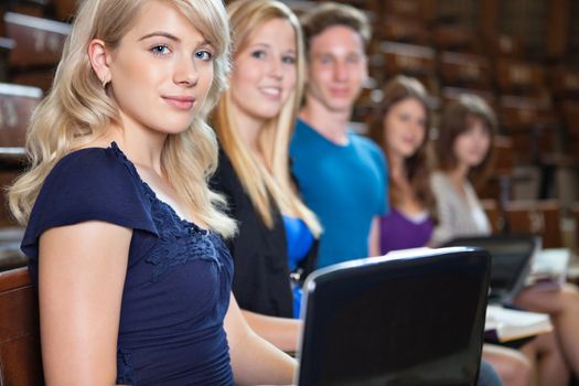 Group of students sitting in a row with laptop and book at seminar hall