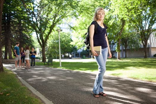 Young blond college girl walking to class with friends in background