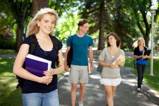 Pretty blond college girl looking at camera with friends in background