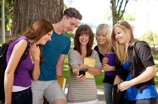 Group of students outdoors looking at a humorous image on a cell phone