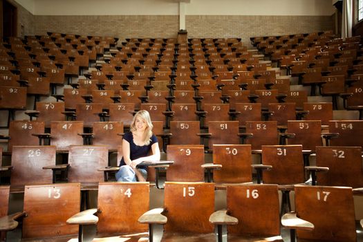 Happy blond college student alone in large lecture hall