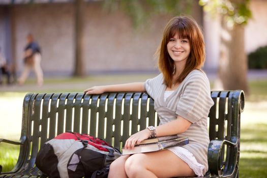 Portrait of a happy young college girl outdoors on a bench