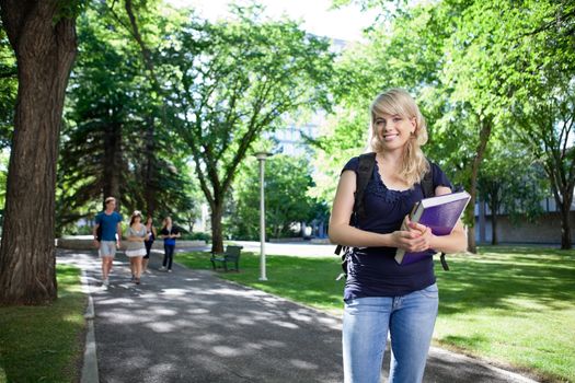 Portrait of smiling college girl holding book while her friends walking in background