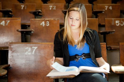 Young college girl looking at text book in lecture hall