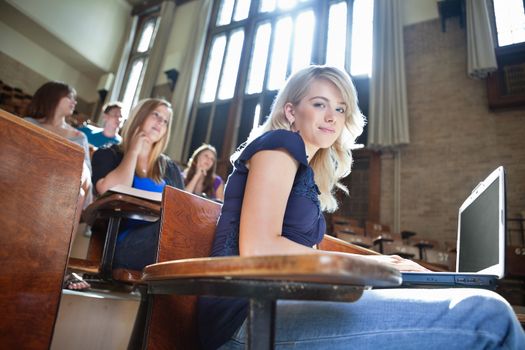Portrait of college girl using laptop while students sitting in background