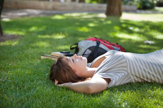 Young college student lying down on grass at campus lawn