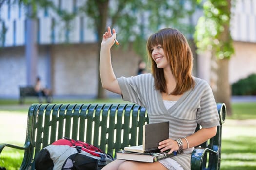 Young smiling college girl waving hand to person outside of image