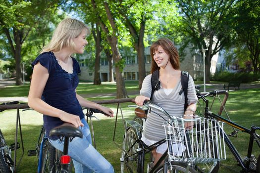 Happy young female students standing with bicycle at college campus lawn