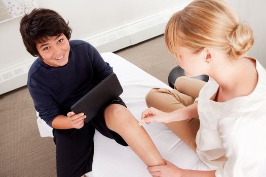 Young male receiving pediatric acupuncture while playing games on a digital tablet