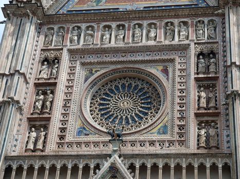 Orvieto Duomo facade.The delicately carved rose window of the facade is surrounded by framed marble bust and life-sized sculptedfigures in gothic niches
